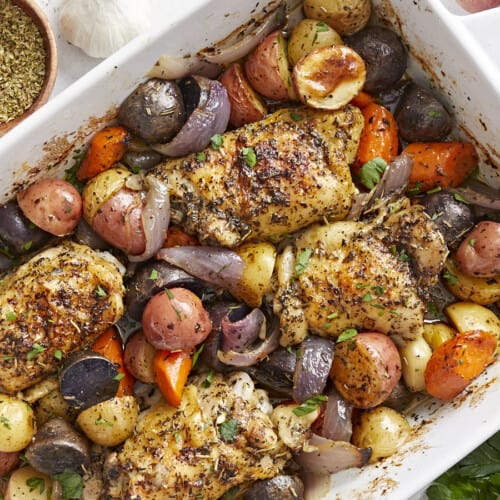 Overhead view of roasted chicken and vegetables in a white casserole dish.