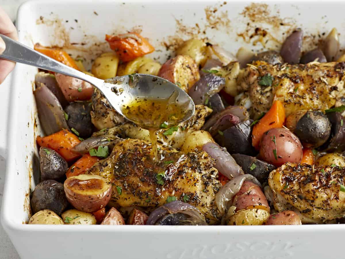 Side view of pan juices being drizzled over the chicken and vegetables. 