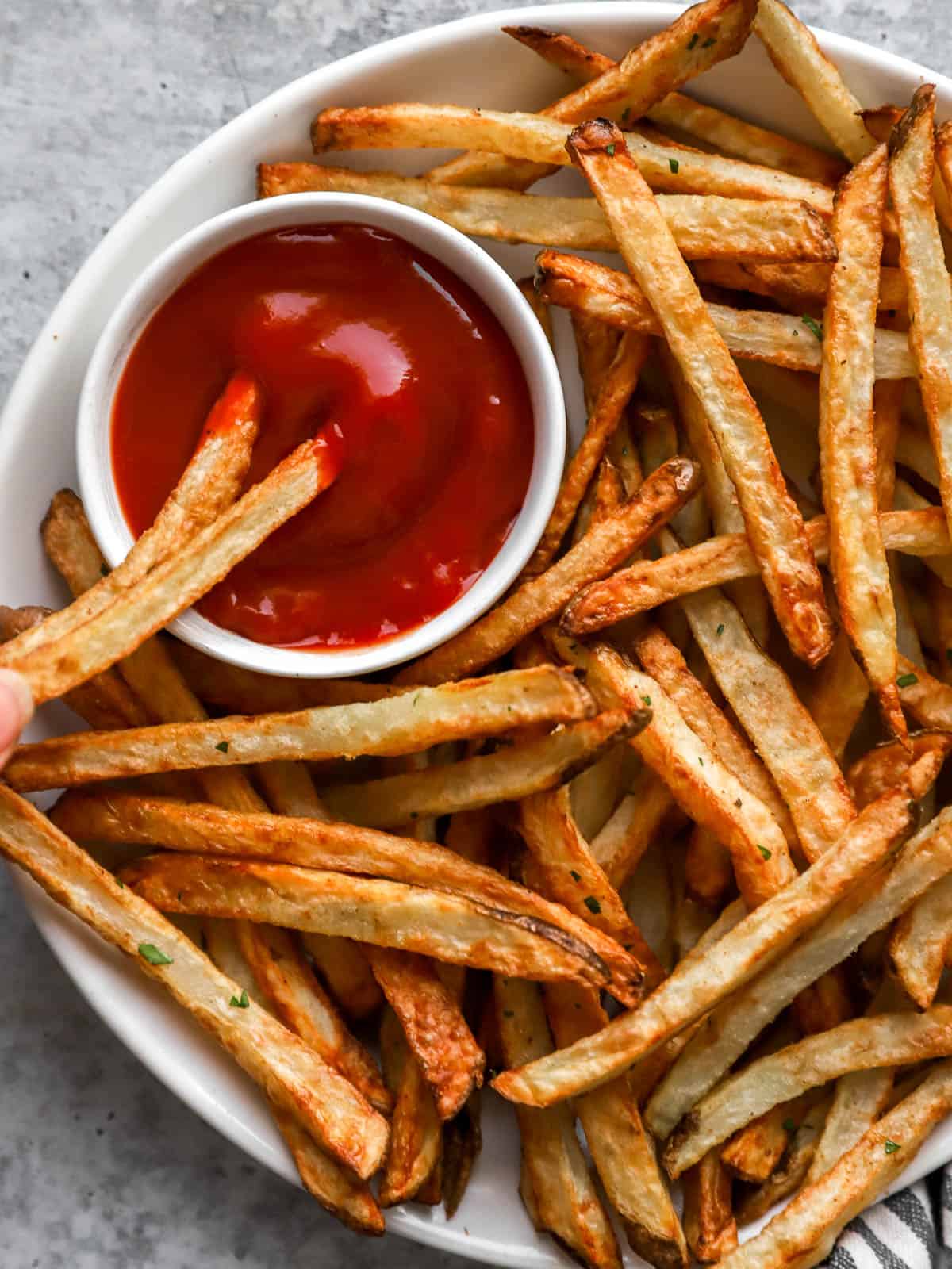 Overhead view of 2 french fries dipped into ketchup on a platter of fries.