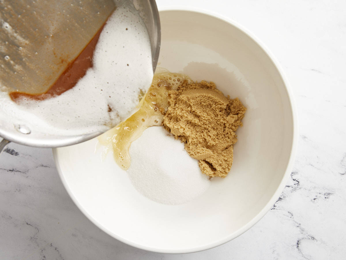 Brown butter being added to white and brown sugar.