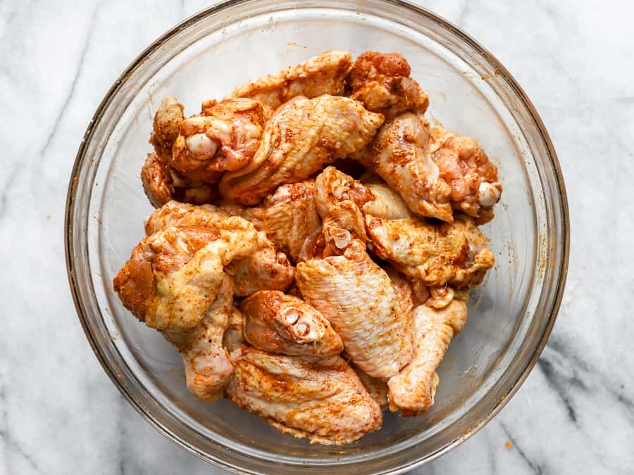 seasoned raw chicken wings in a glass bowl.