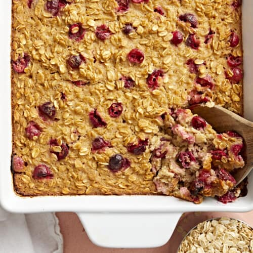 Baked oatmeal being scooped out of the casserole dish with a wooden spoon.