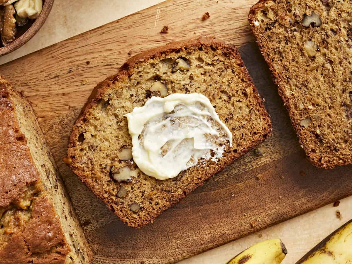 Overhead view of a slice of banana bread with butter spread on it. 