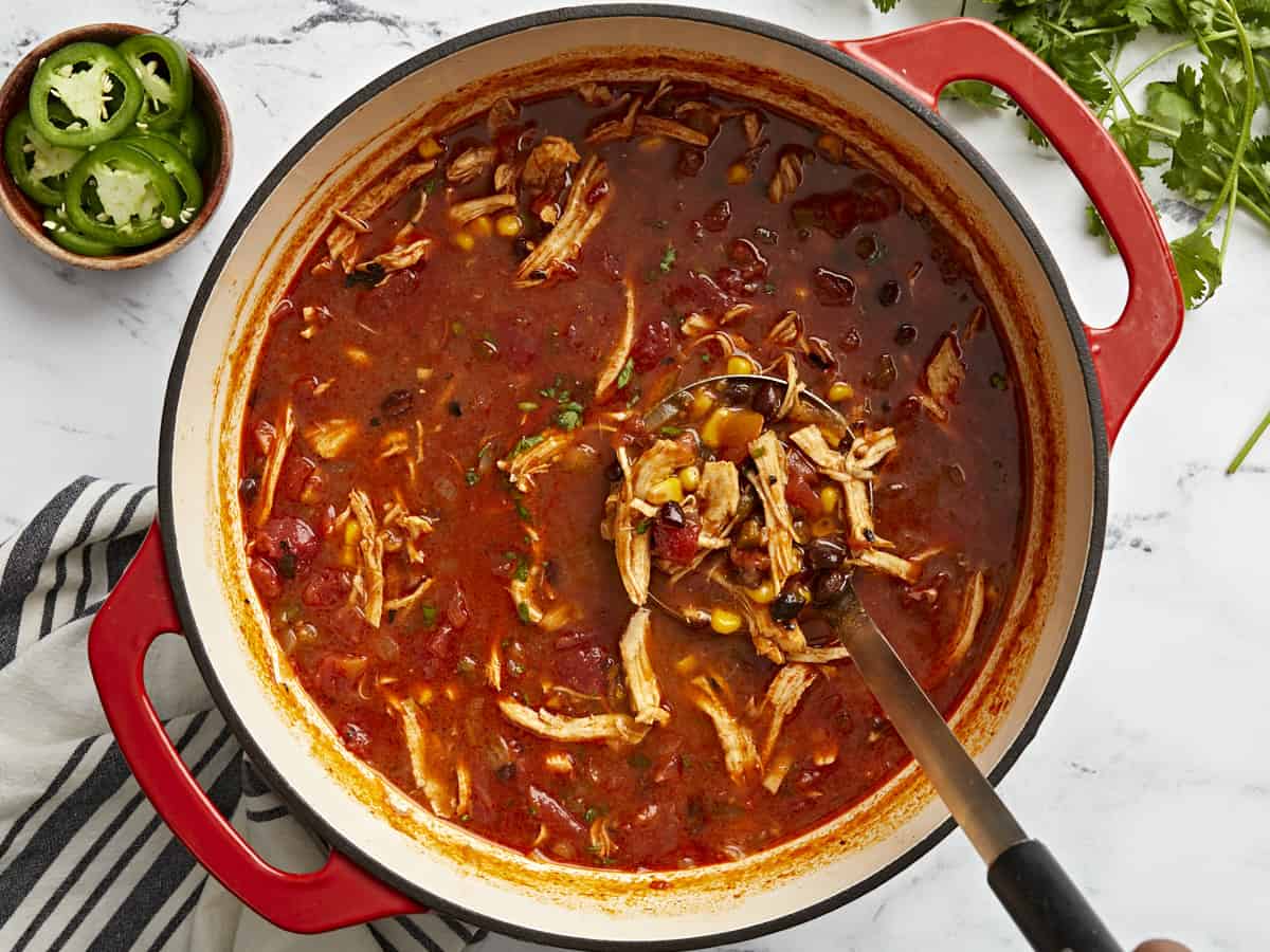 Overhead view of chicken enchilada soup in a dutch oven with a ladle scooping some soup out.