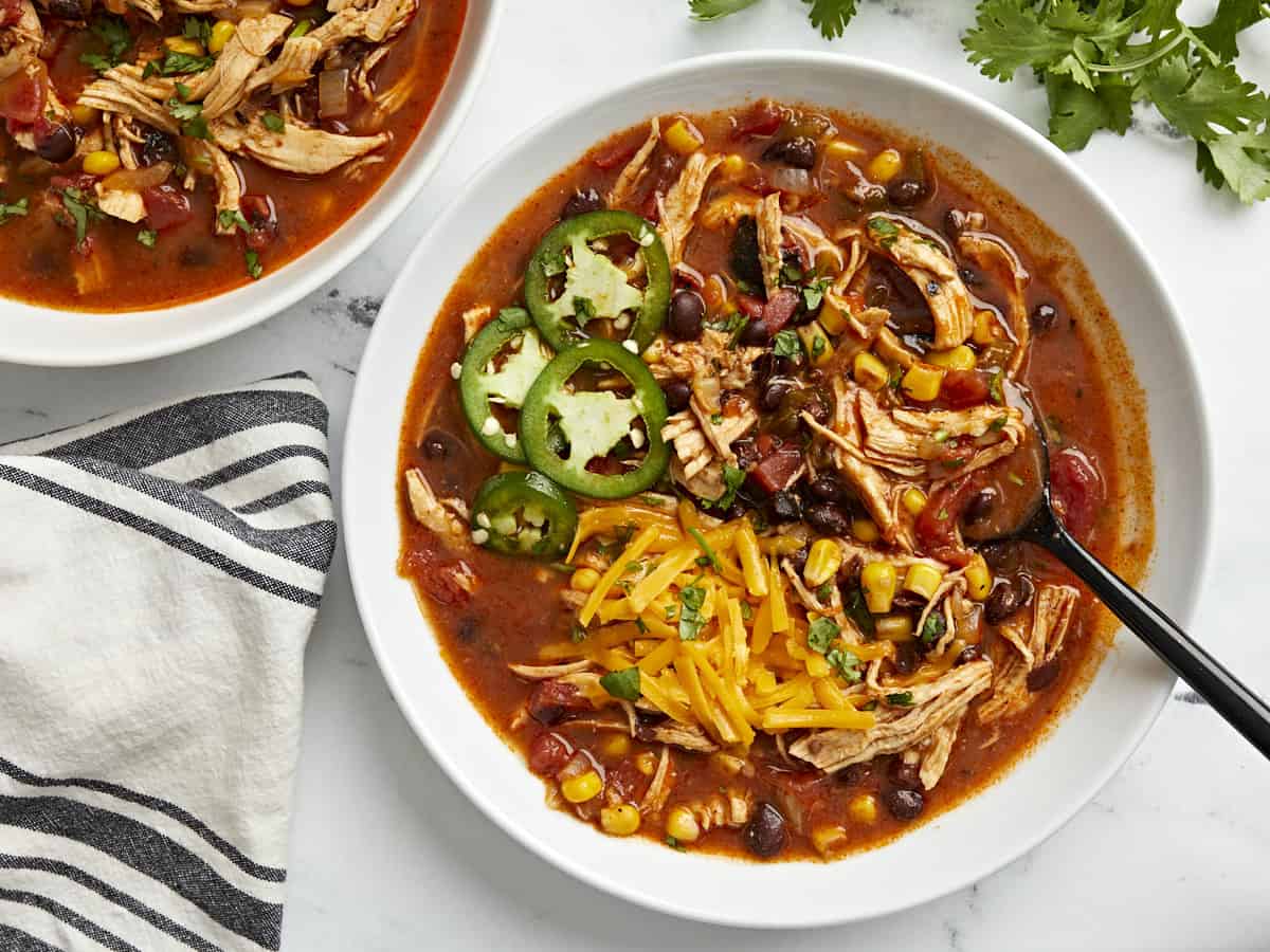 Overhead view of two bowls of chicken enchilada soup with jalapeno and shredded cheese on top.