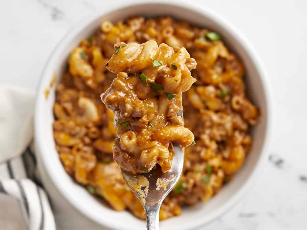 Close up of chili mac on the fork held over a bowl. 