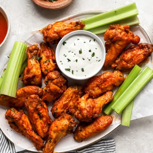 overhead view of buffalo wings on a white platter with celery and white sauce.