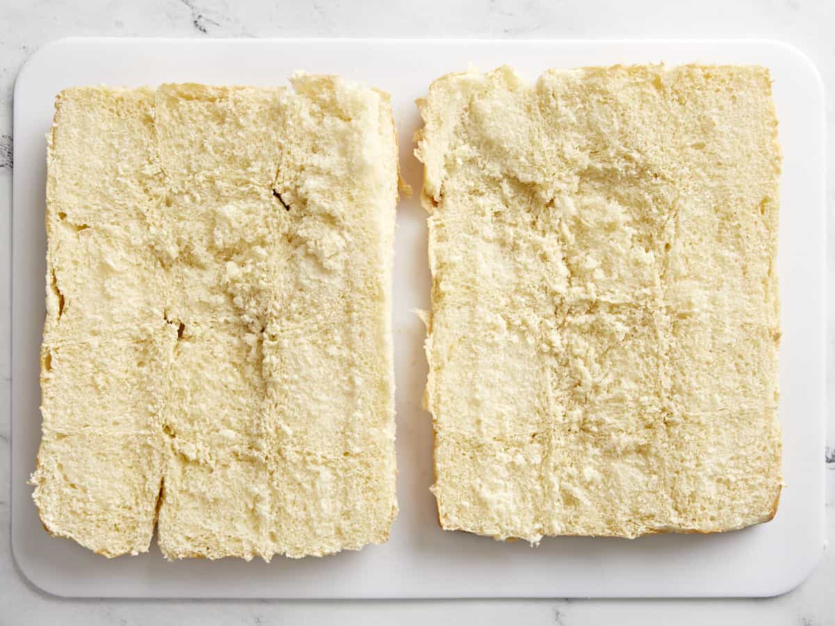 Overhead view of 12 hawaiian rolls cut in half on a cutting board.