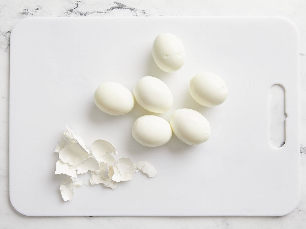 Six hard boiled eggs peeled on a cutting board.