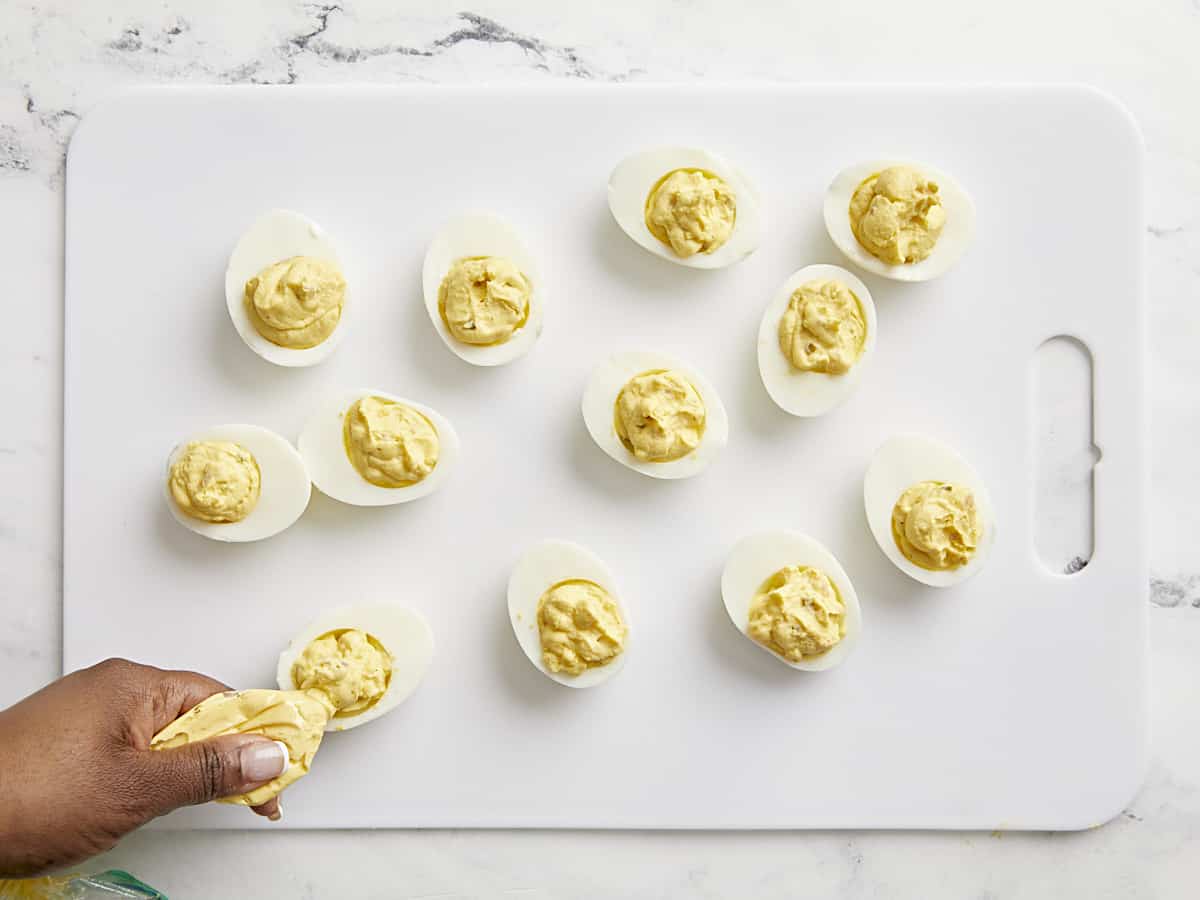 Hard boiled eggs cut in half with deviled egg ingredients being pipped inside.