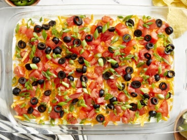 Overhead view of 7 layer dip in a glass casserole dish with a napkin, chips, and lime wedges on the side.