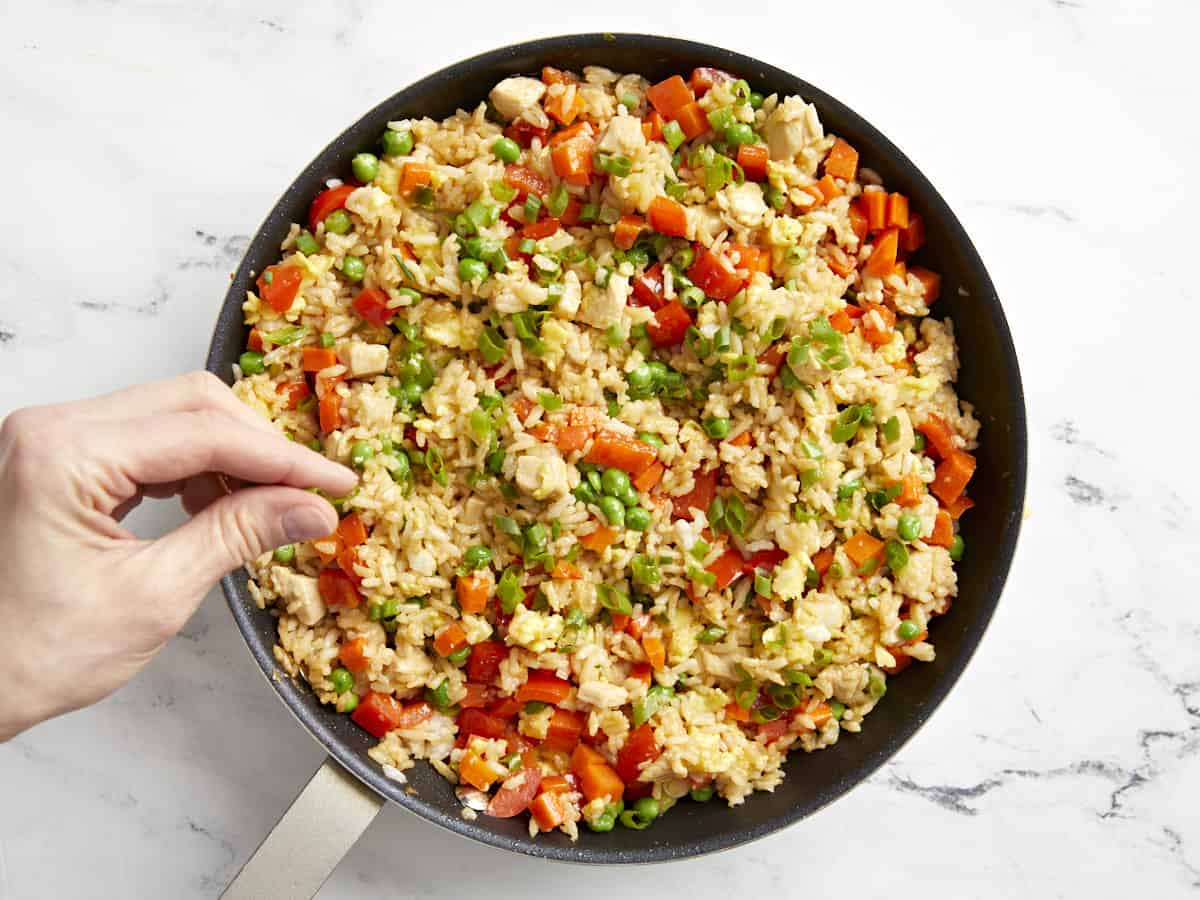 sprinkling salt over chicken fried rice in a frying pan.