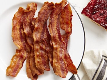 Overhead view of Air Fryer bacon strips on a white serving plate with toast on the side.