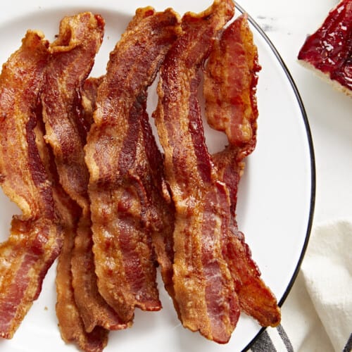 Overhead view of Air Fryer bacon strips on a white serving plate with toast on the side.