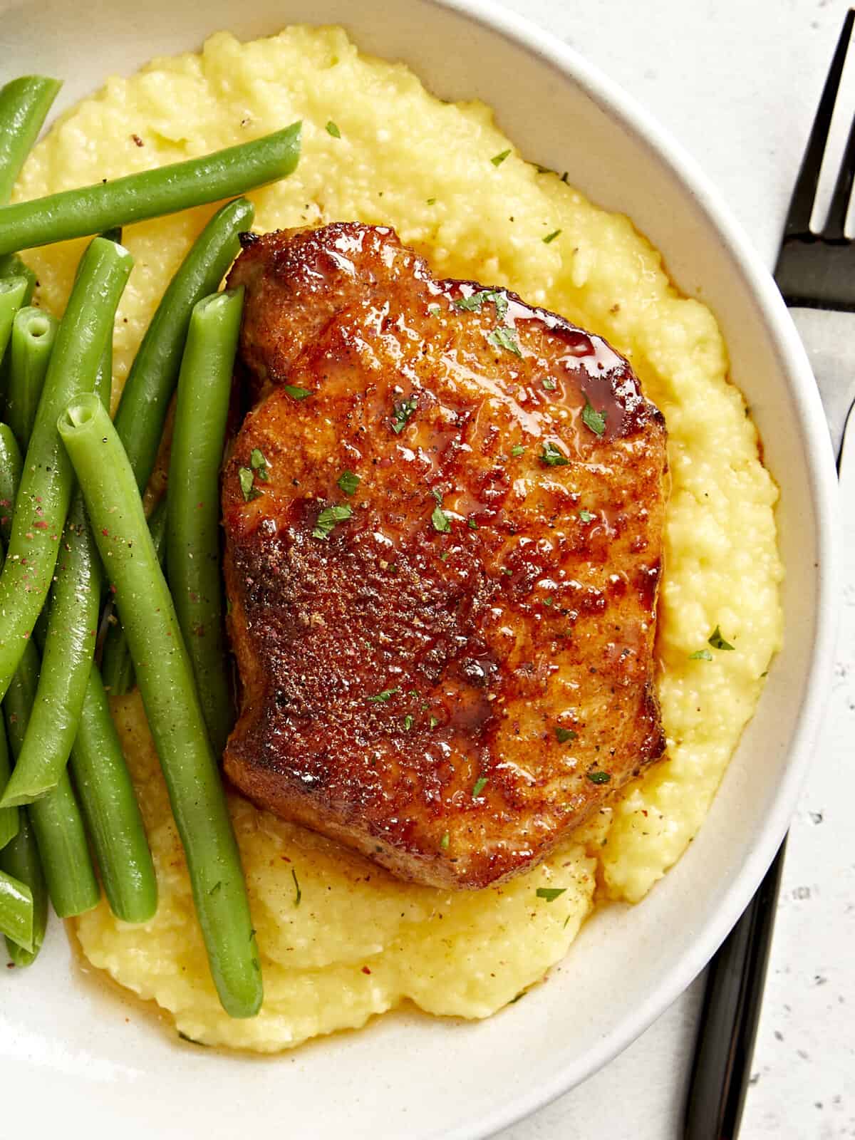 partial overhead view of an air fryer pork chop on a white plate with potatoes and green beans.