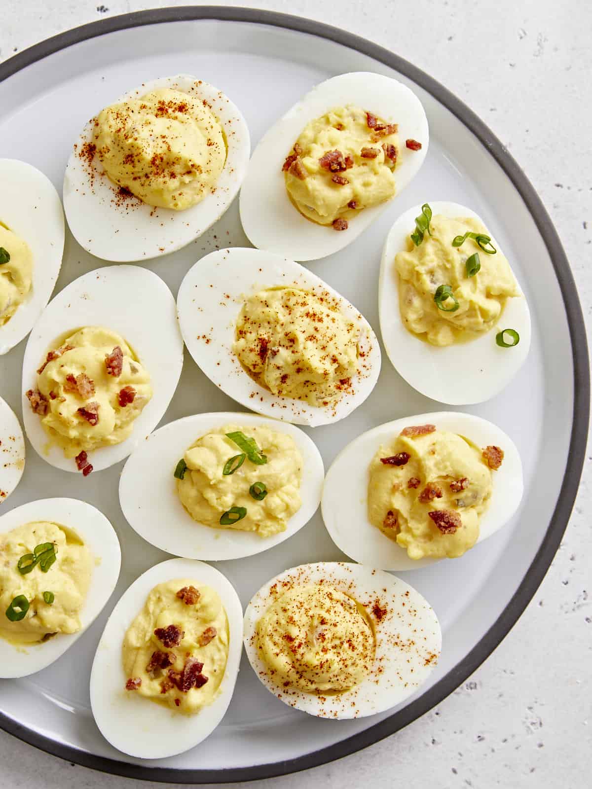 Overhead view of deviled eggs on a platter with different toppings.