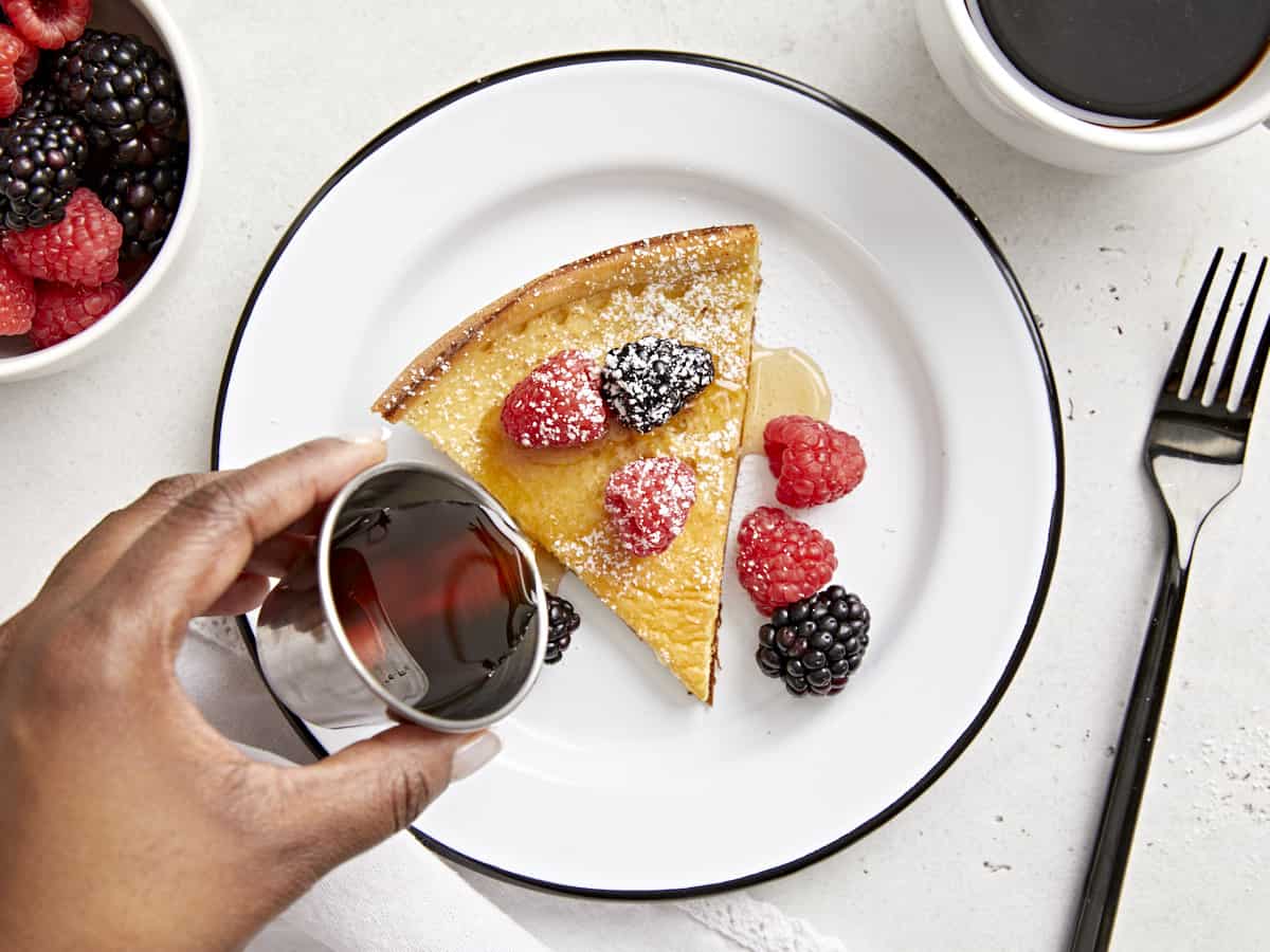 Overhead view of a slice of dutch baby on a plate with maple syrup being poured on top.