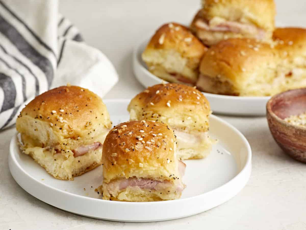 Side view of two serving plates of ham and cheese sliders with a napkin on the side.