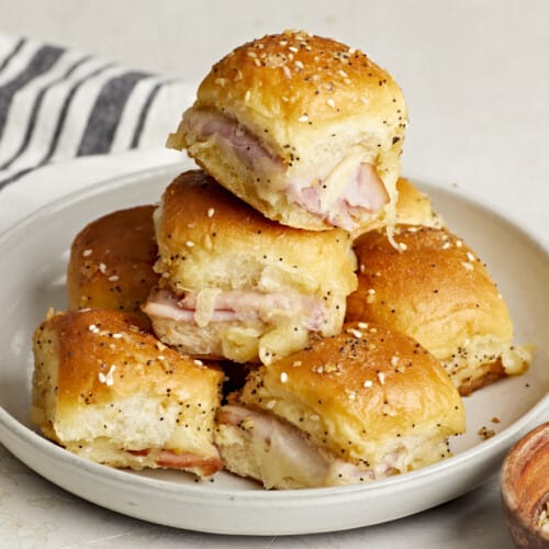 Front side view of a stack of ham and cheese sliders on a plate.