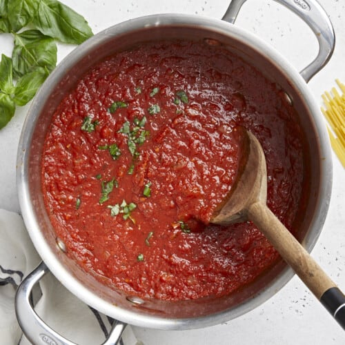 Overhead view of finished marinara sauce in the pot surrounded by pasta and herbs.