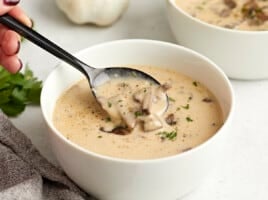 Side view of a bowl of creamy mushroom soup with a spoon lifting some out of the bowl.