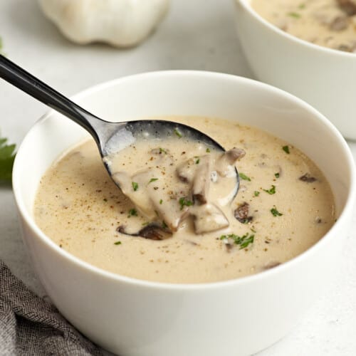 Side view of a bowl of creamy mushroom soup with a spoon lifting some out of the bowl.