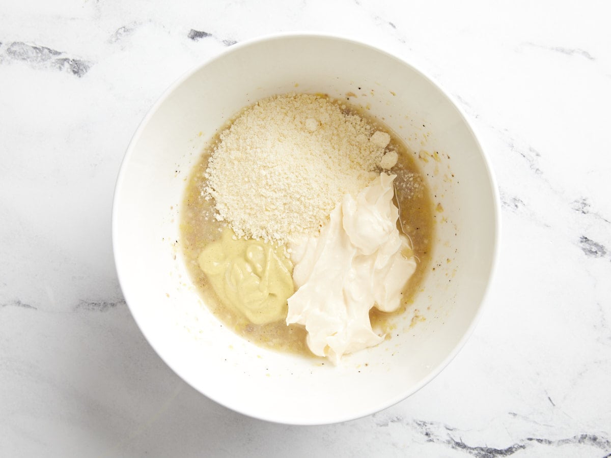 Parmesan and mayo added to Caesar dressing in a bowl.