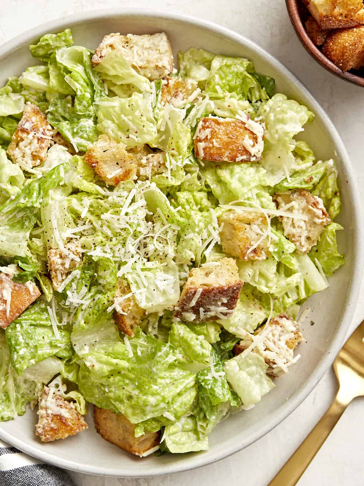 Overhead view of a plate of caesar salad with a gold fork on the side.