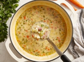 a ladleful of ham and potato soup suspended over a pot of soup.