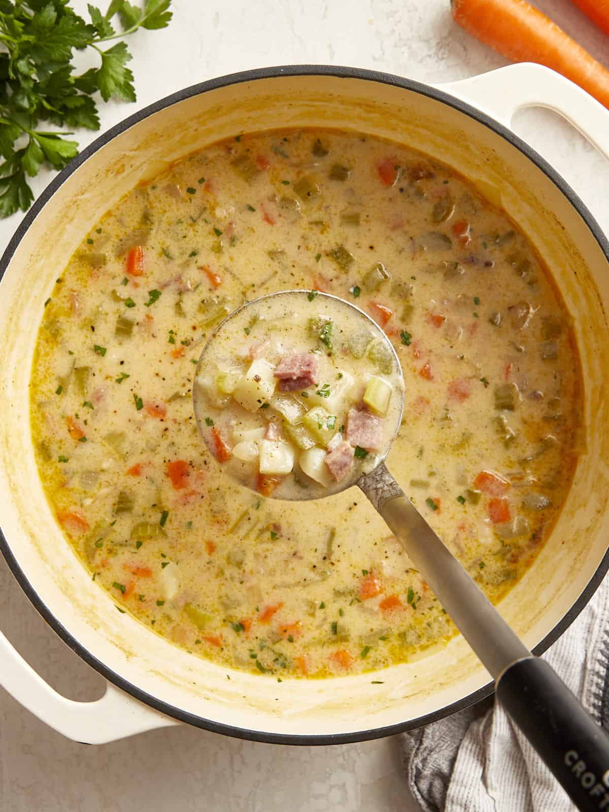 a ladleful of ham and potato soup suspended over a pot of soup.