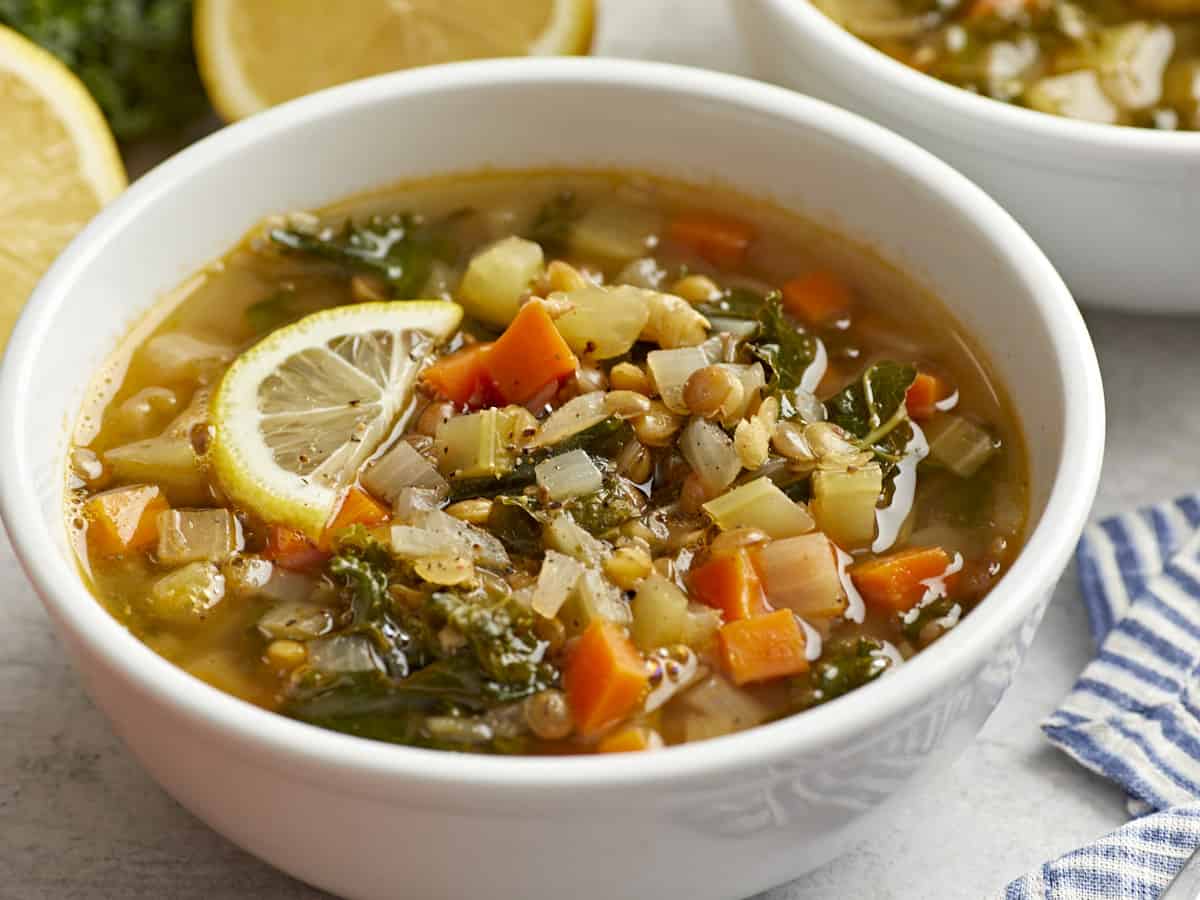 three-quarters view of mediterranean lentil soup in a white bowl with a lemon slice.