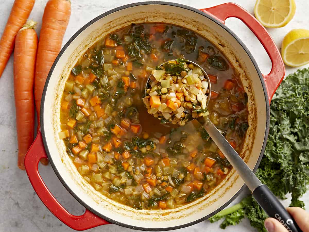 overhead view of a spoon lifting a scoop of mediterranean lentil soup from a red dutch oven.