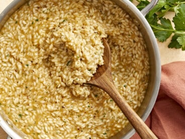 overhead view of a wooden spoon in a pan of parmesan risotto.