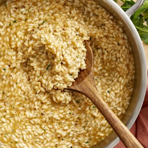 overhead view of a wooden spoon in a pan of parmesan risotto.