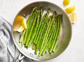 overhead view of sauteed asparagus in a frying pan with lemon wedges.