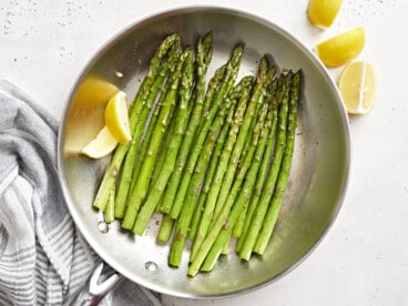 overhead view of sauteed asparagus in a frying pan with lemon wedges.