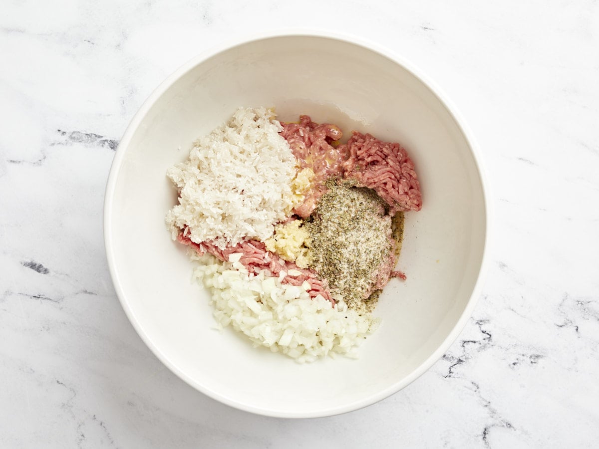 Meat and ingredients for porcupine meatballs added to a large bowl.