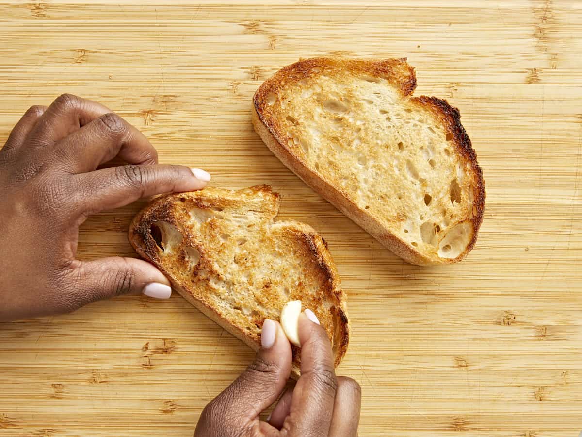 Toasted sourdough bread with a garlic clove being rubbed over the top.