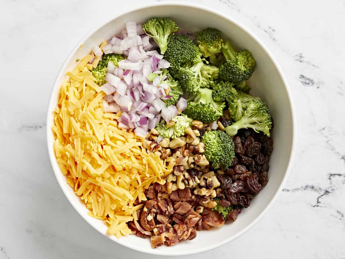 ingredients for broccoli salad in a white bowl.