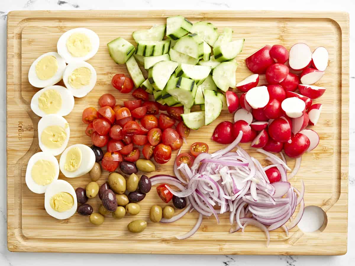 overhead view of prepped ingredients for nicoise salad on a cutting board.