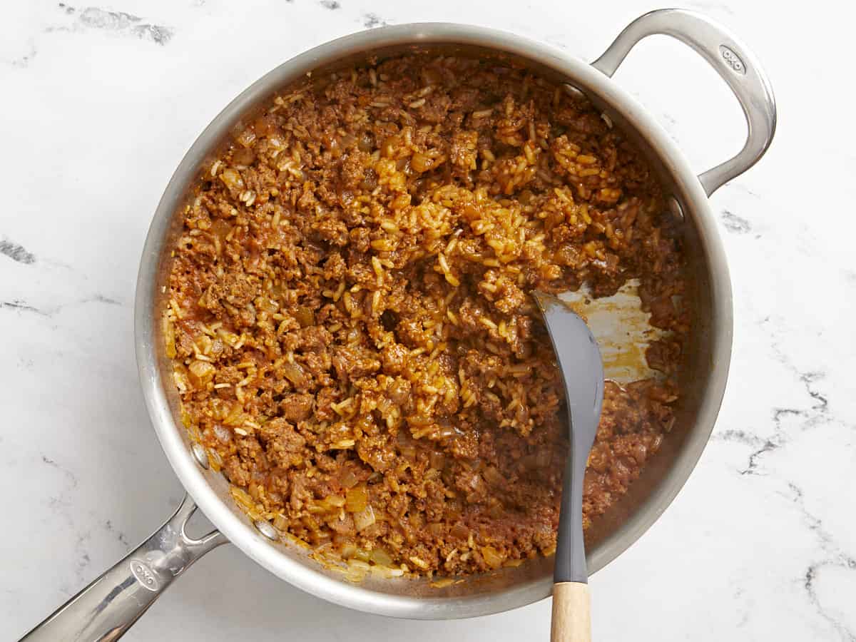 Cooked chorizo and rice in the skillet being scooped to the side with a spoon.