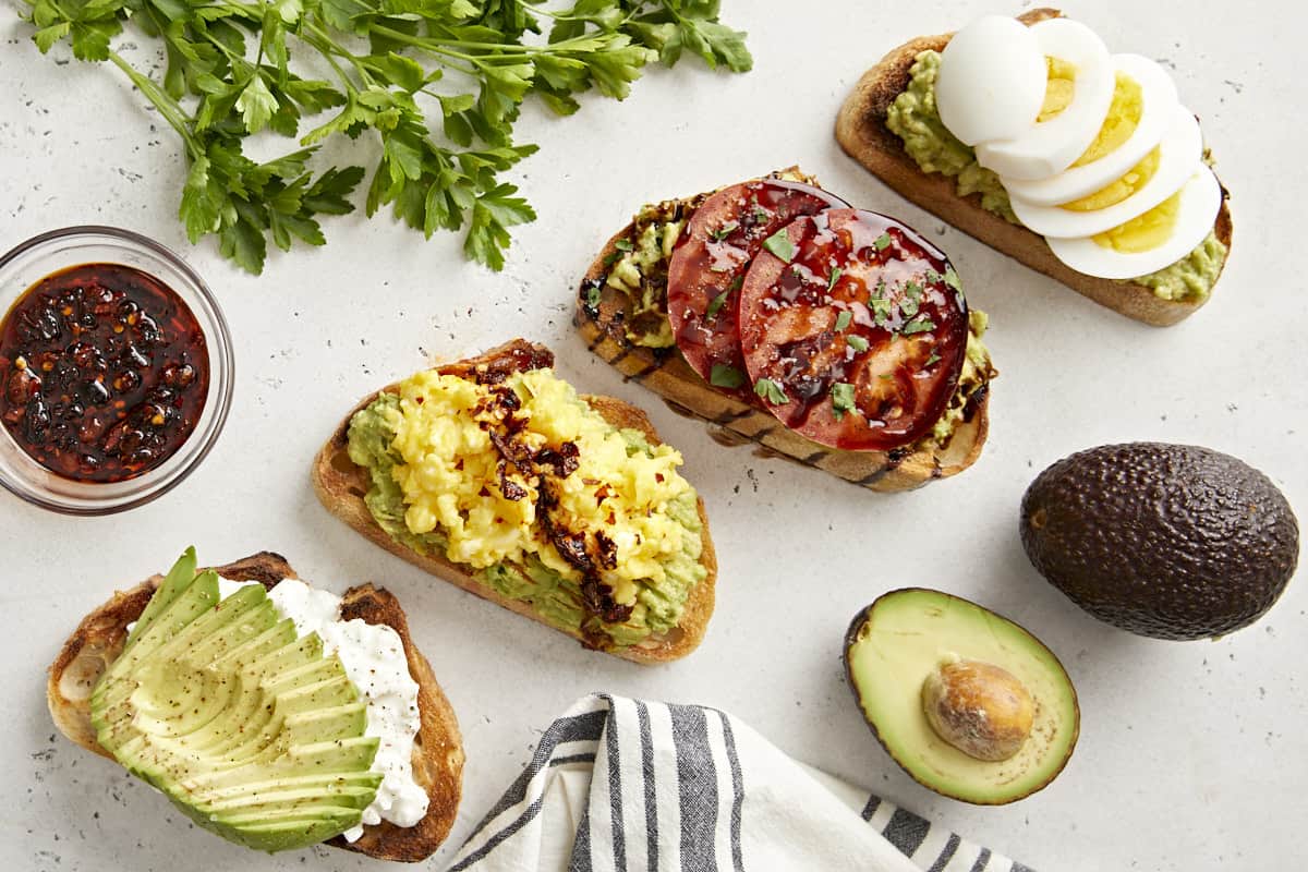 Overhead view of avocado toast made 4 different ways with parsley, avocado, and a napkin on the side.