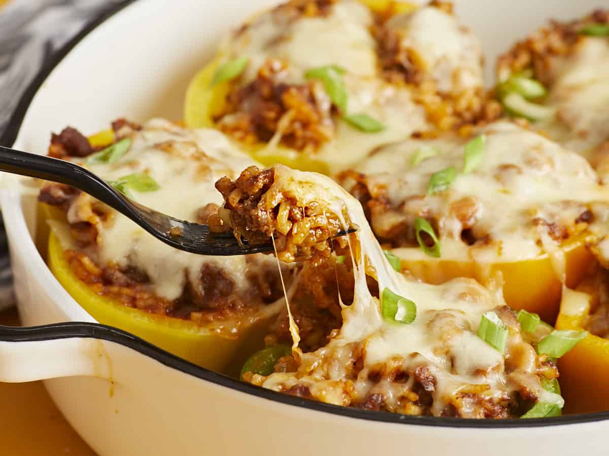 Side view of a fork lifting some stuffing out of the bell pepper with the cheese pulling. 