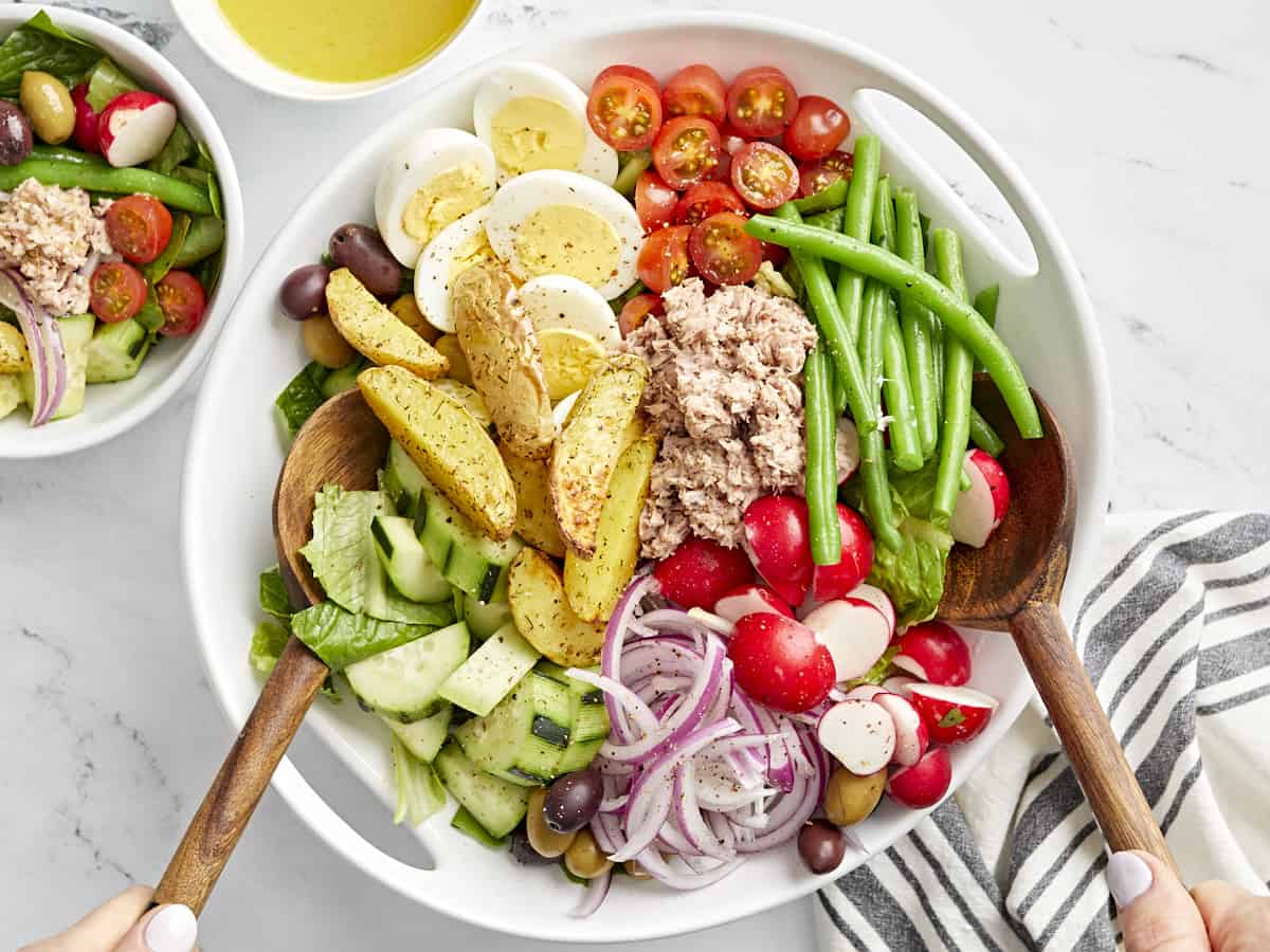 nicoise salad in a white bowl with wooden salad spoons.