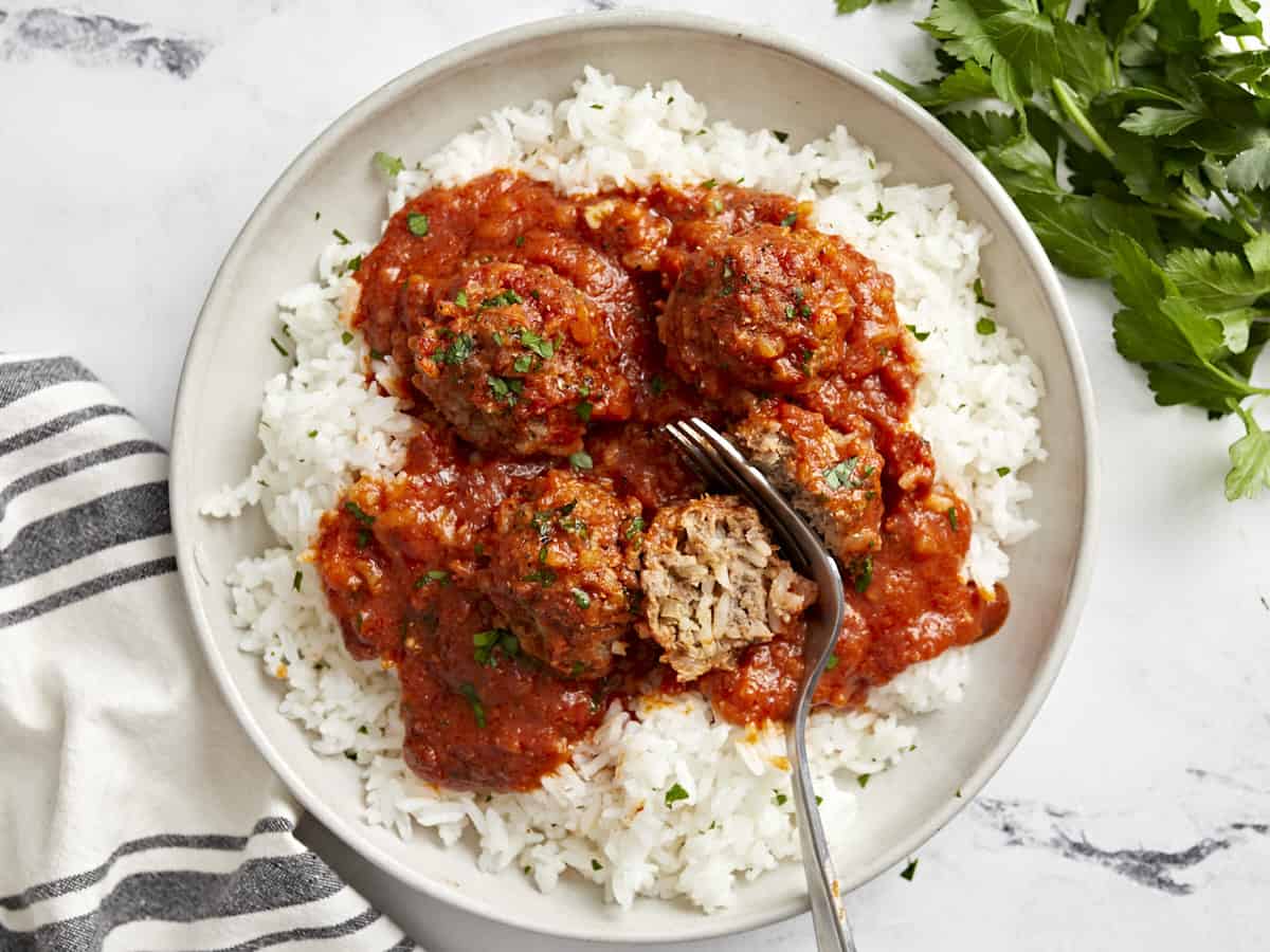 Overhead view of porcupine meatballs on a serving plate with white rice and a fork cutting a meatball in half.