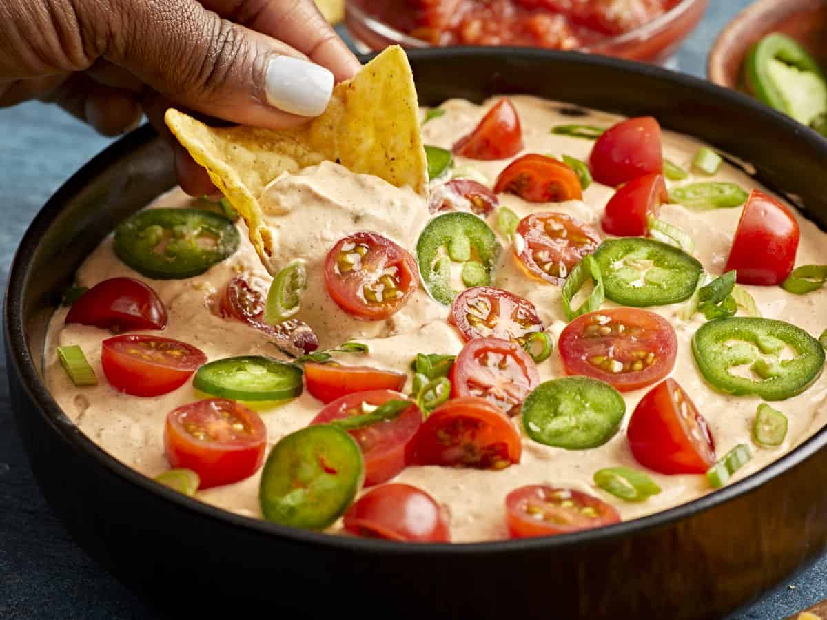 Side view of a hand scooping some taco dip with a tortilla chip.