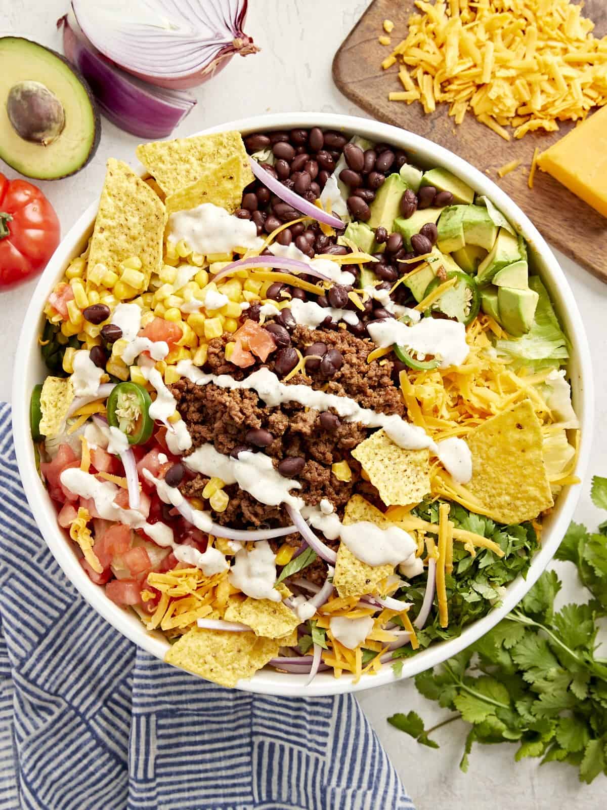 overhead view of taco salad with creamy white dressing and corn chips in a white bowl.