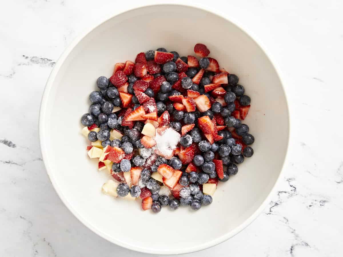 cut fruits tossed with sugar in a white bowl.