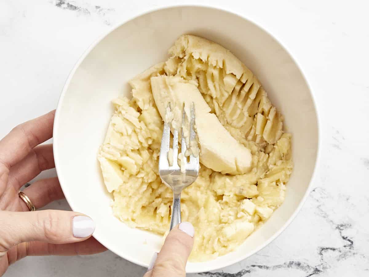 mashing bananas in a white bowl with a fork.