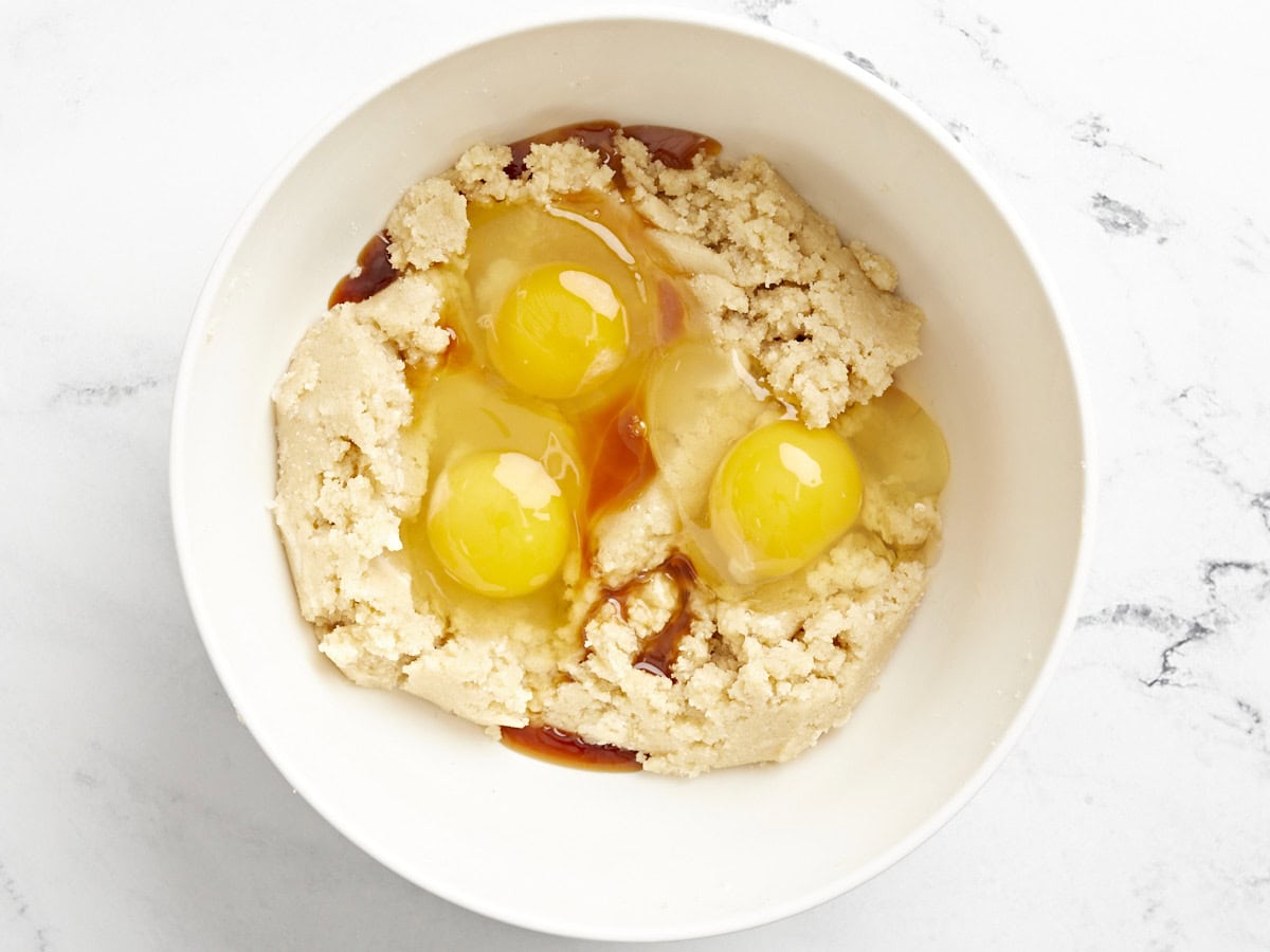 eggs added to creamed butter and sugar in a white bowl.